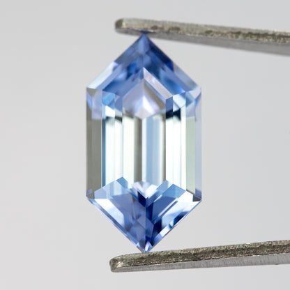 Upright blue long-hexagon sapphire in tweezers, with bright long reflections running through the center.
