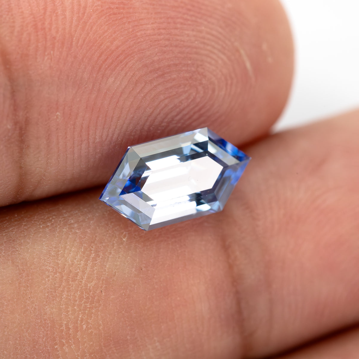 Blue long-hexagon lab-grown sapphire resting on fingertips, showing the face and its scale against the skin.