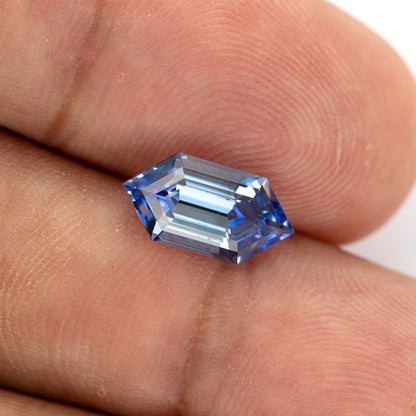 The blue step-cut sapphire resting diagonally on fingertips, with its complete outline visible.