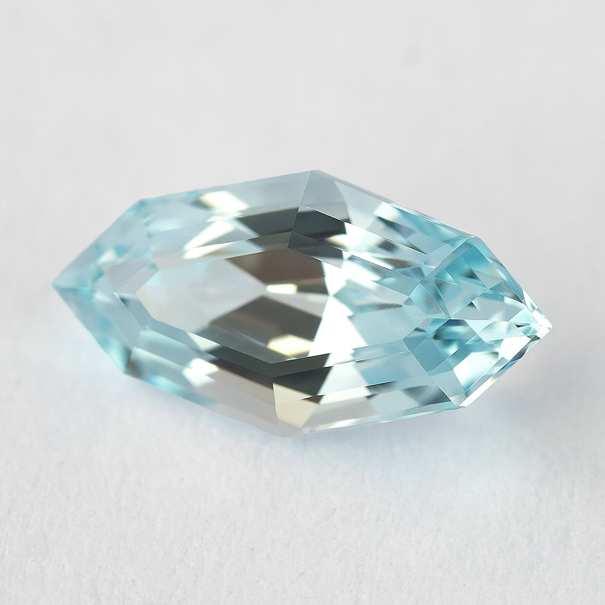 A marquise-shaped, step-cut, light blue lab-grown sapphire angled slightly on a white background.