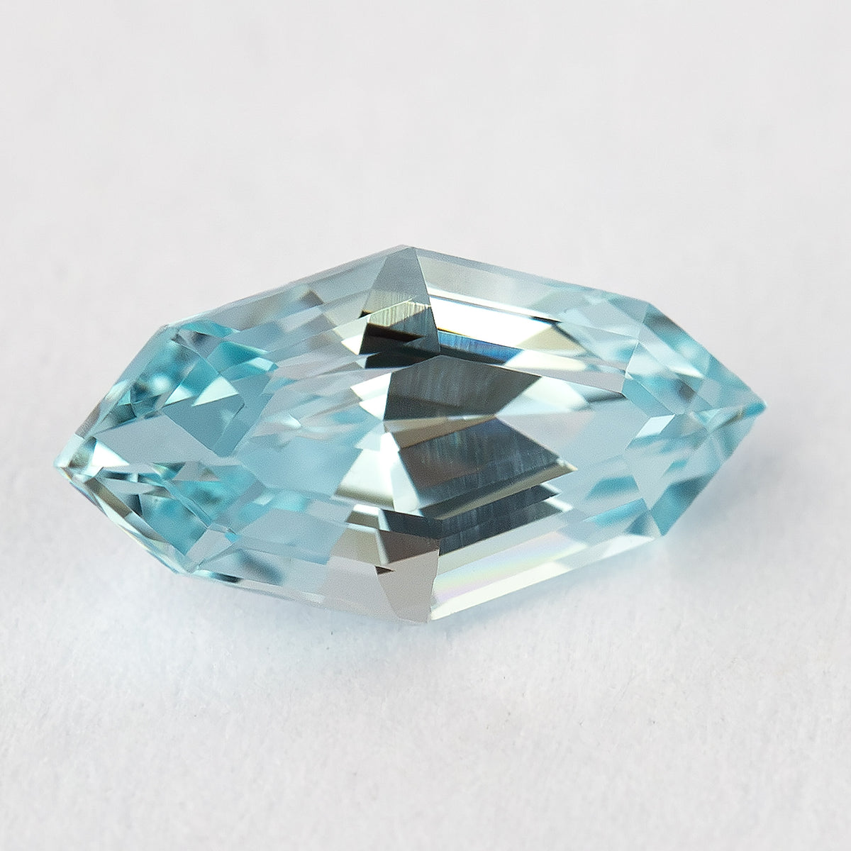 Light blue marquise step-cut lab-grown sapphire at a face-up tilt on a white surface, with dark central step reflections.