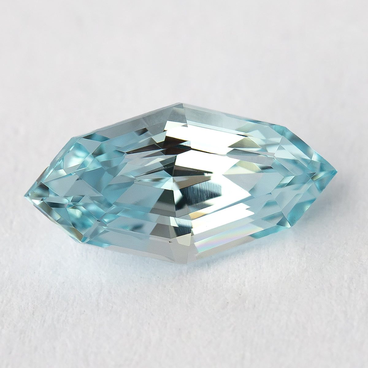 A marquise-shaped, step-cut, light blue lab-grown sapphire angled on a white background.