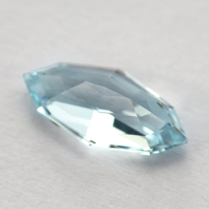 Oblique pavilion-side view of the light blue marquise step-cut lab-grown sapphire resting on a white surface.