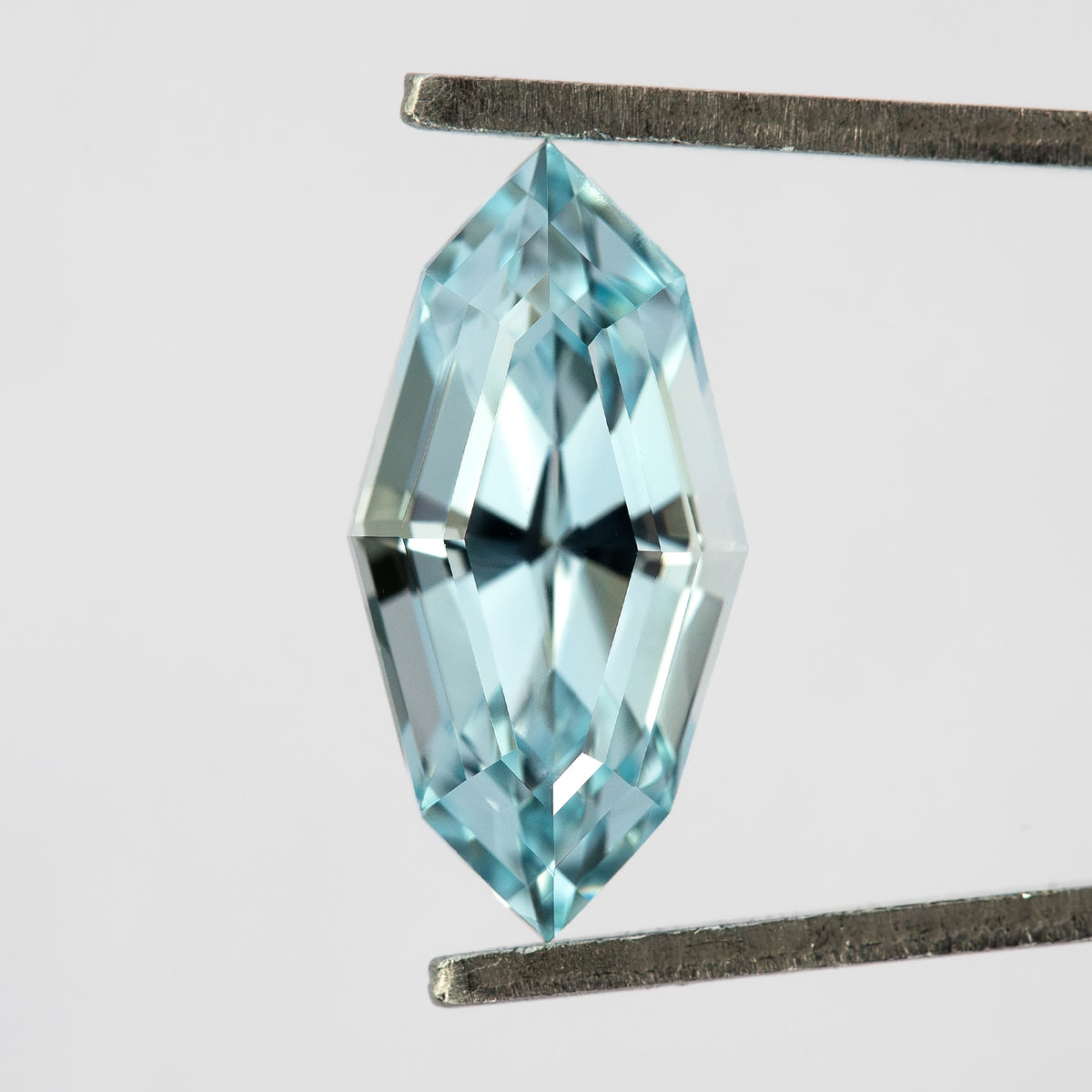 Light blue step-cut lab-grown sapphire held face-up vertically in tweezers.