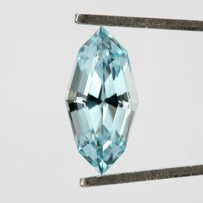 Light blue step-cut lab-grown sapphire held face-up vertically in tweezers.