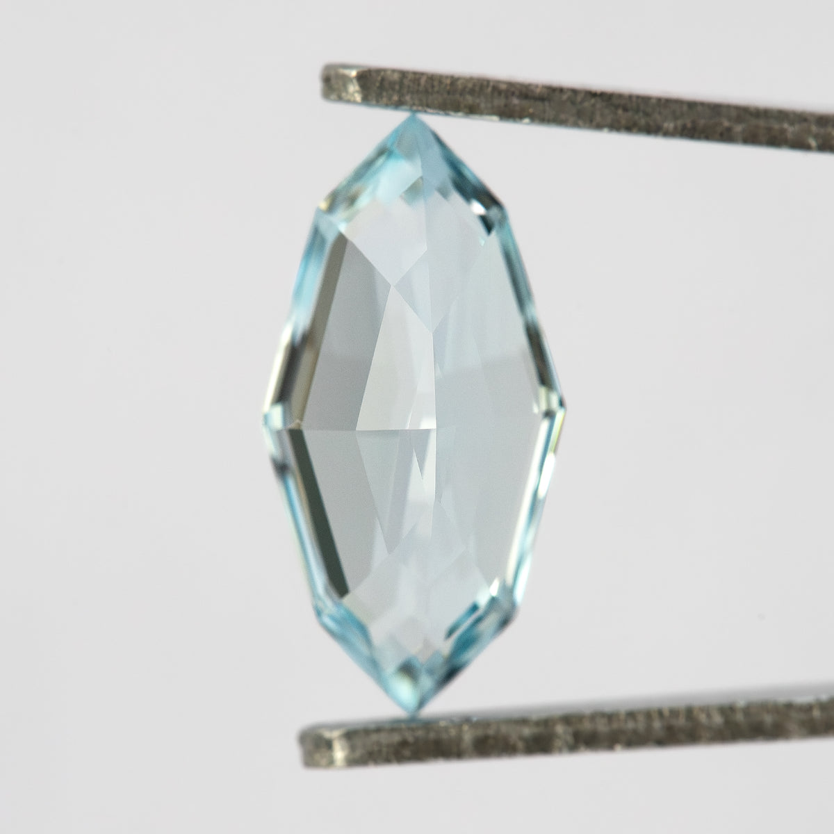 Reverse view of the aquamarine blue / light blue sapphire showing pavilion facets in tweezers.