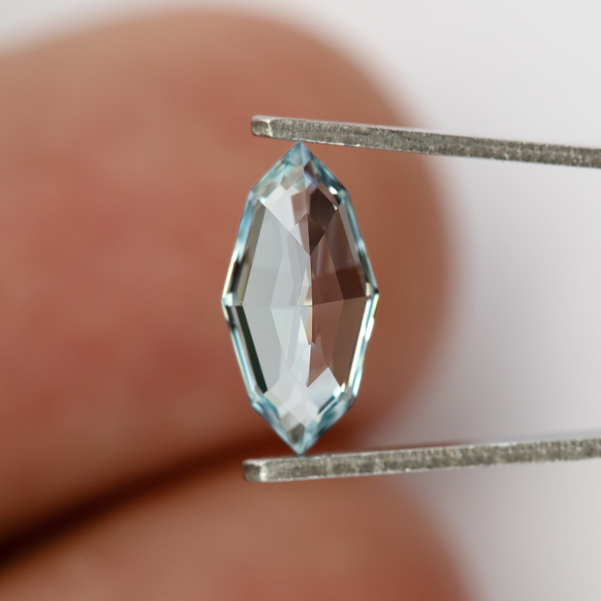 Pavilion-side view of the light blue marquise step-cut lab-grown sapphire in tweezers against a fingertip for scale.