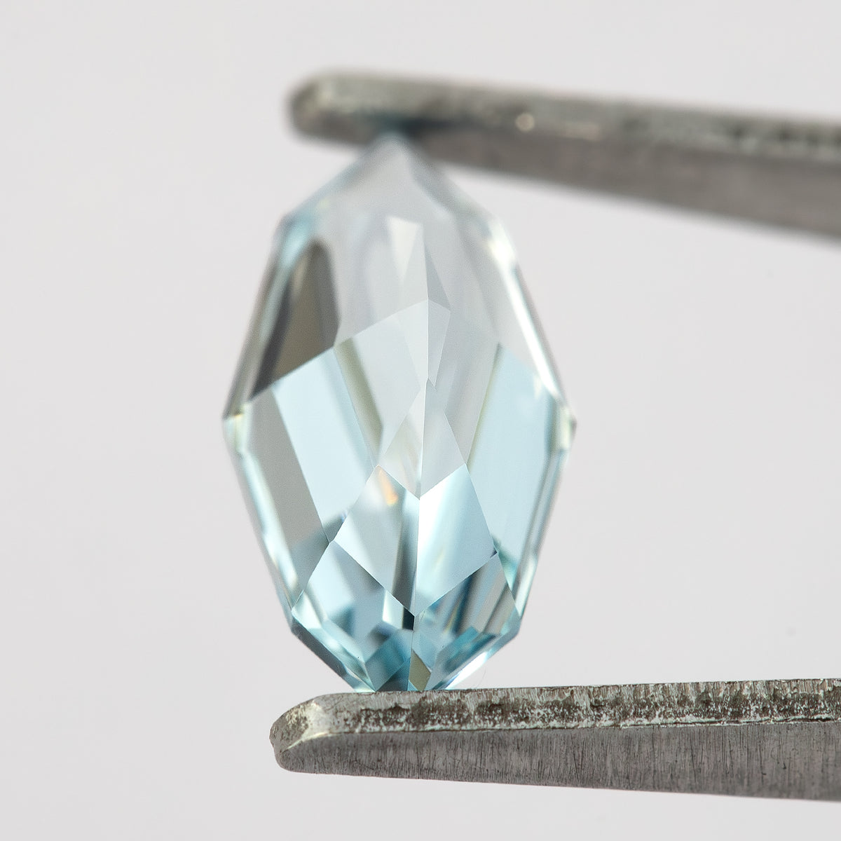 Oblique pavilion-side view of the light blue marquise step-cut lab-grown sapphire held diagonally in tweezers.