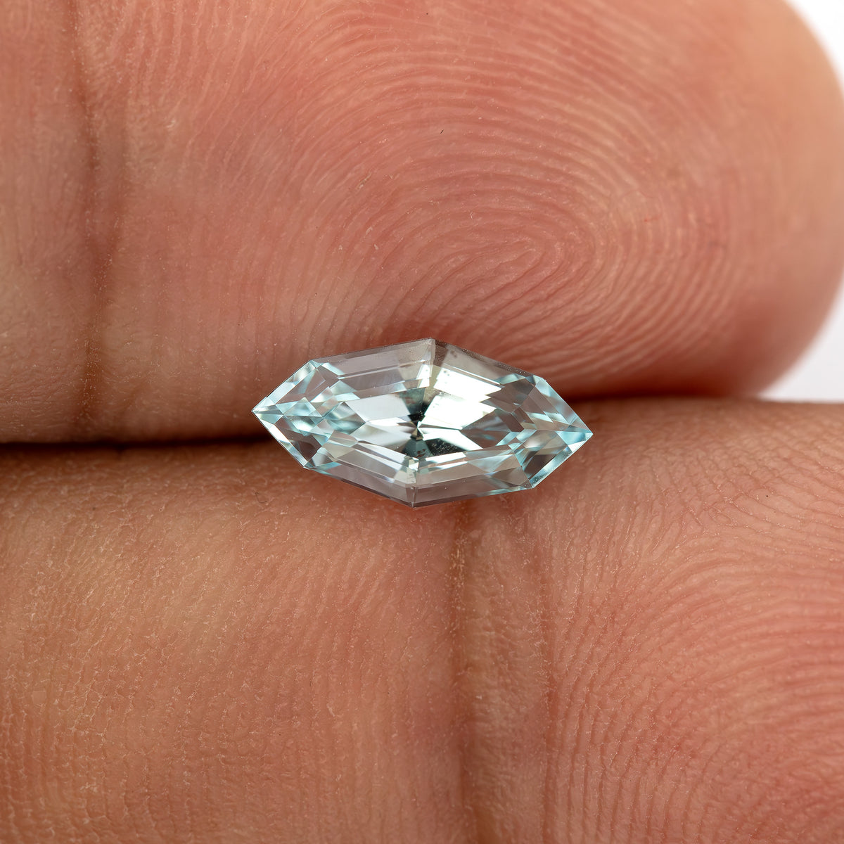 Light blue step-cut lab-grown sapphire resting on fingertips for scale.