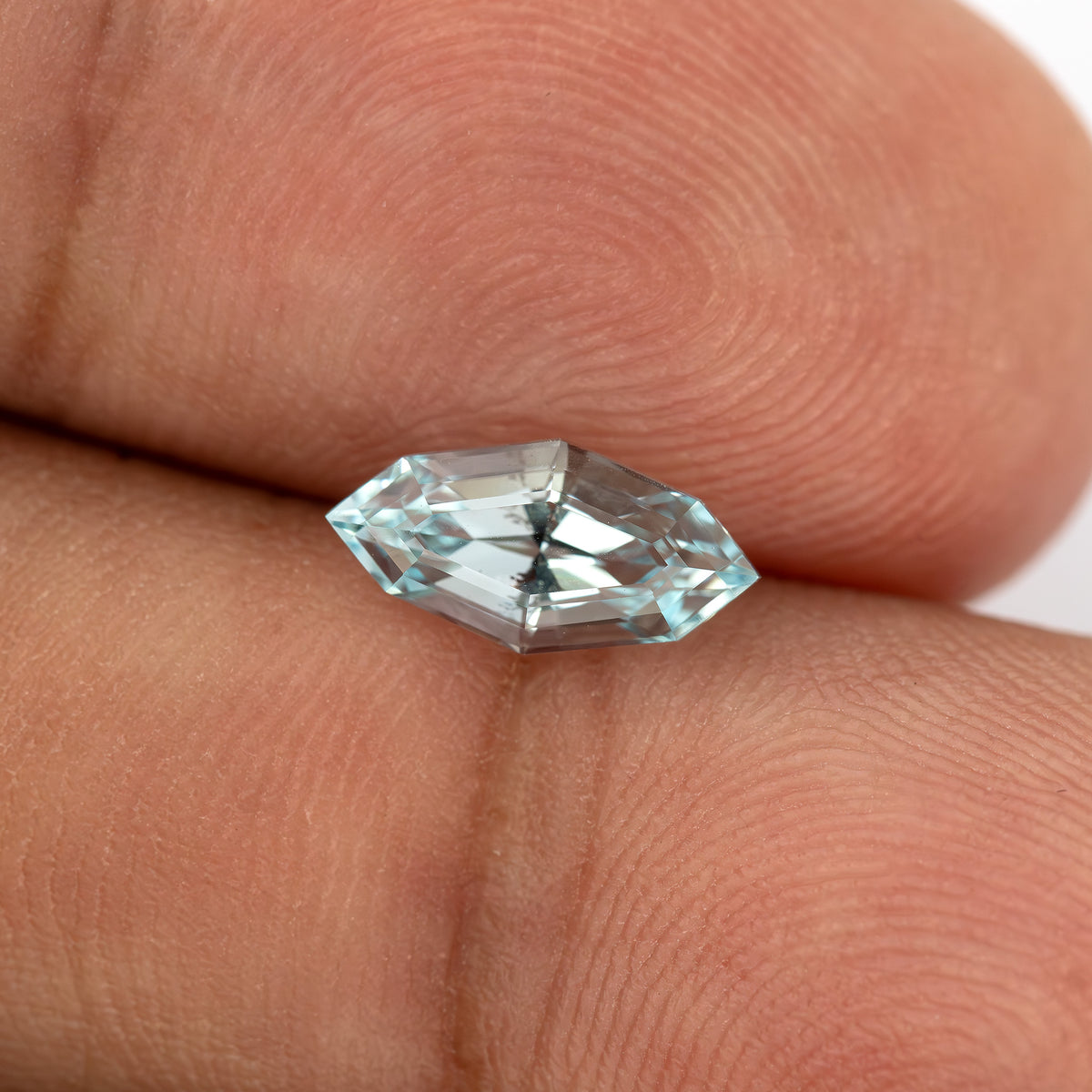 Light blue marquise step-cut lab-grown sapphire resting horizontally against fingertips, with bright white and dark central reflections.