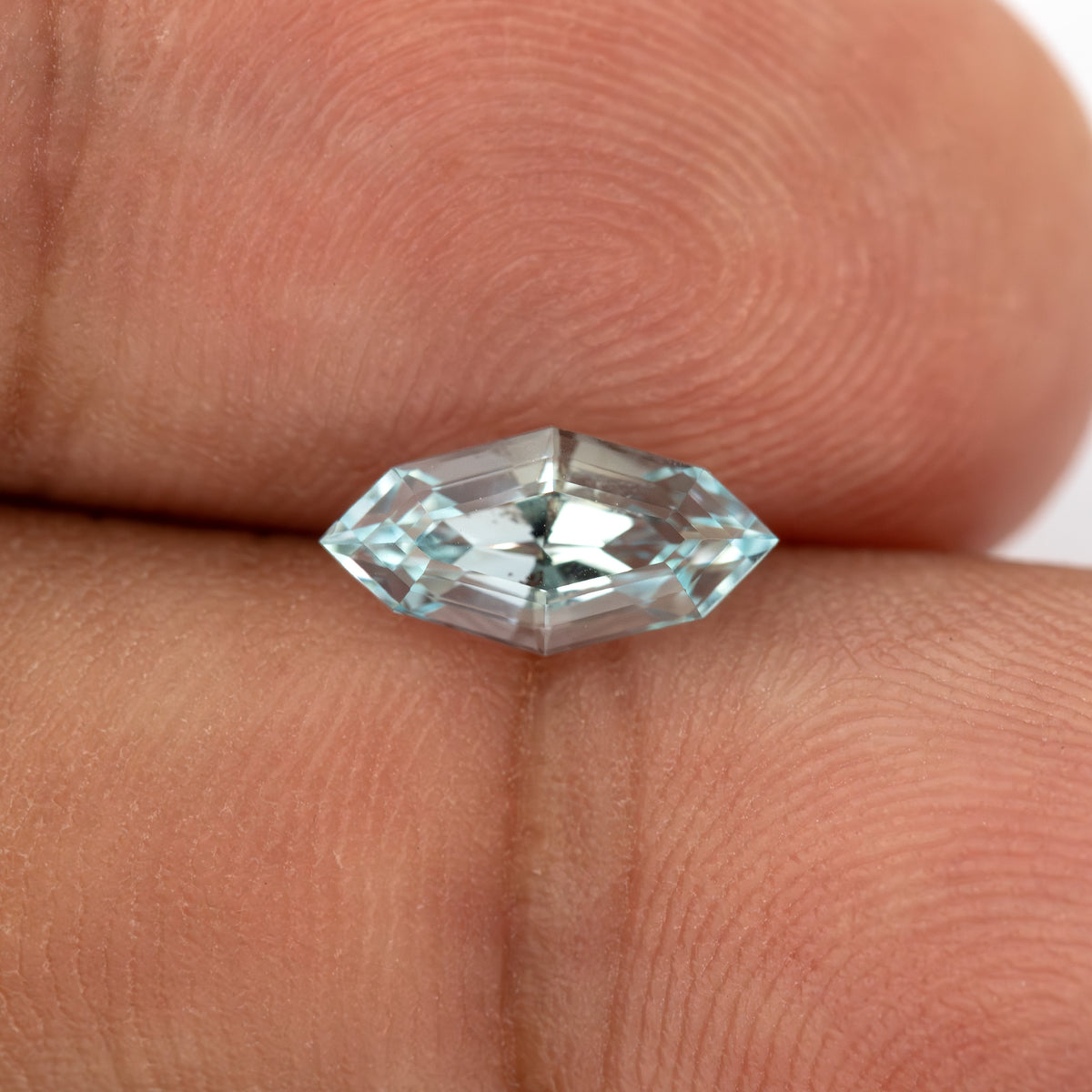 Light blue marquise step-cut lab-grown sapphire tilted against fingertips, showing pale blue edges and reflective central steps.