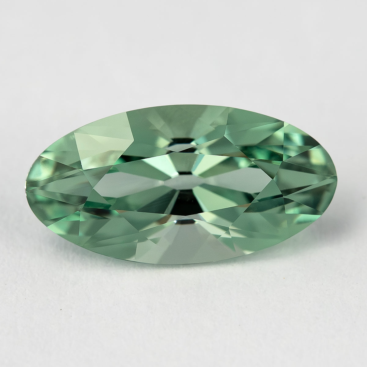 Mint-green lab-grown sapphire face-up on a pale surface, showing the elongated outline and broad crown facets.