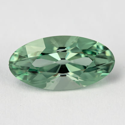 Mint-green lab-grown sapphire face-up on a pale surface, showing the elongated outline and broad crown facets.