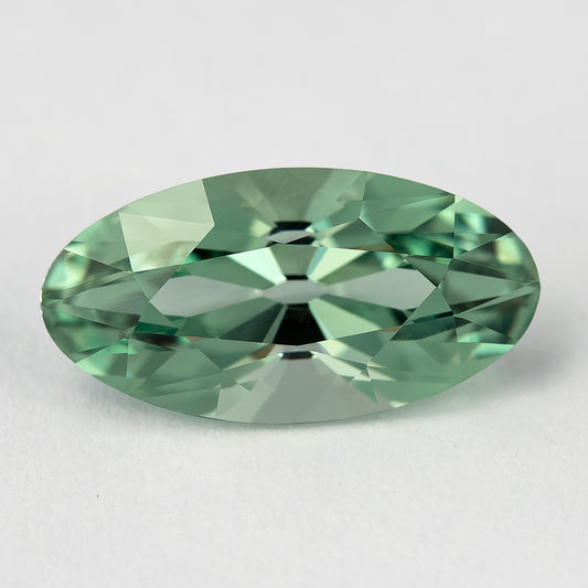 Mint-green lab-grown sapphire face-up on a pale surface, showing the elongated outline and broad crown facets.