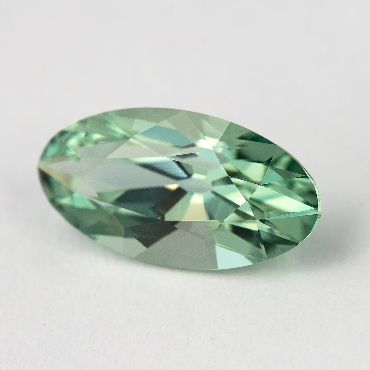 Mint-green lab-grown sapphire tilted on a pale surface, with darker and lighter reflections across its crown.
