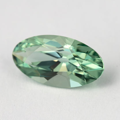 Mint-green lab-grown sapphire tilted on a pale surface, with darker and lighter reflections across its crown.