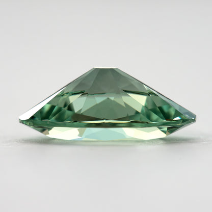Side profile of the mint-green lab-grown sapphire on a pale surface, showing the raised crown and pavilion.