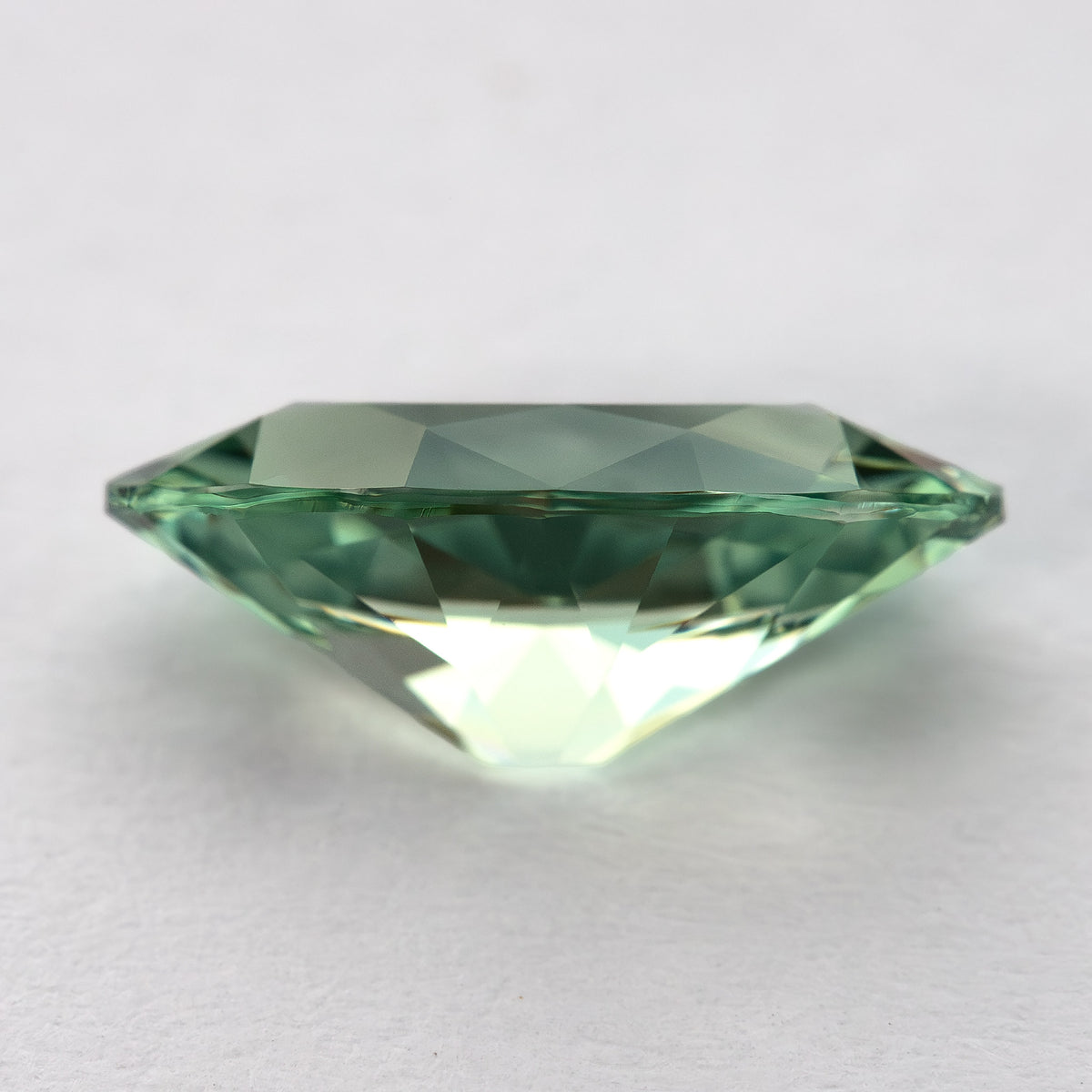 Mint-green lab-grown sapphire in side view, with a dark girdle line and bright lower facets.