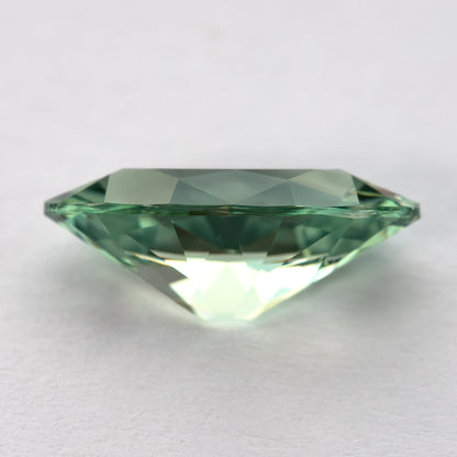 Mint-green lab-grown sapphire in side view, with a dark girdle line and bright lower facets.