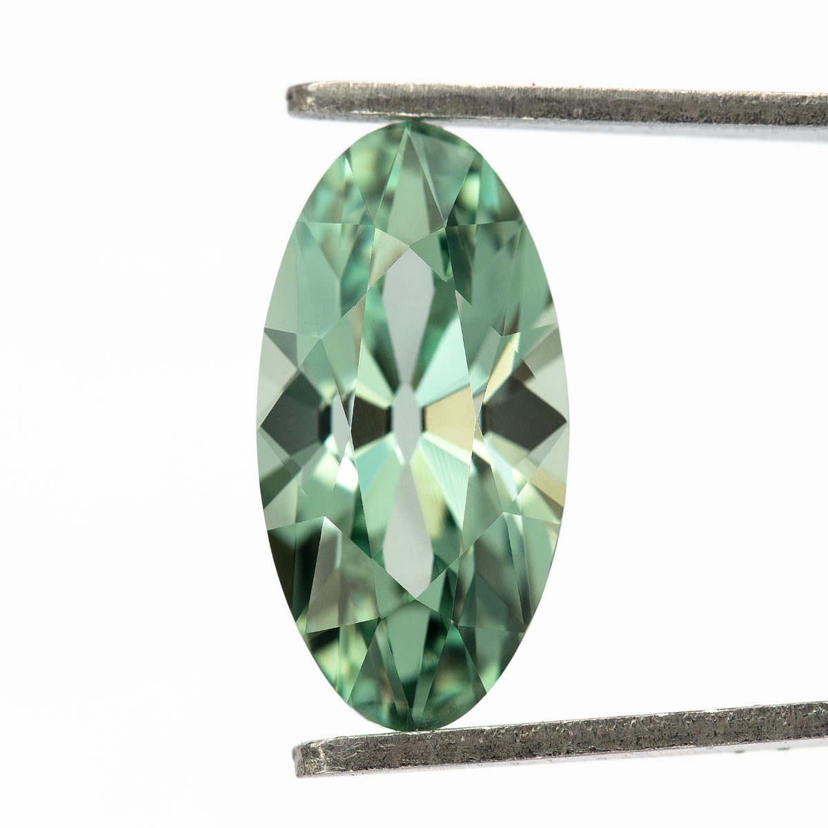 Mint-green lab-grown sapphire held vertically in tweezers, with the crown facets and full elongated outline visible.
