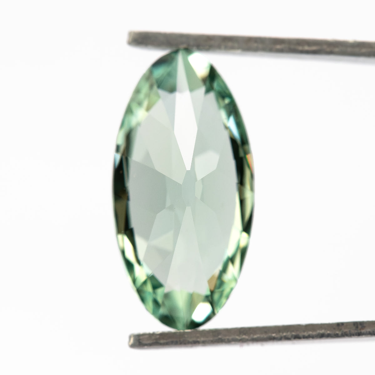 Mint-green lab-grown sapphire turned backward in tweezers, revealing pale reflections across its pavilion.