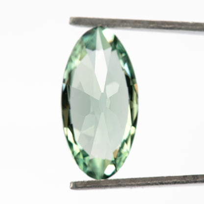 Mint-green lab-grown sapphire turned backward in tweezers, revealing pale reflections across its pavilion.