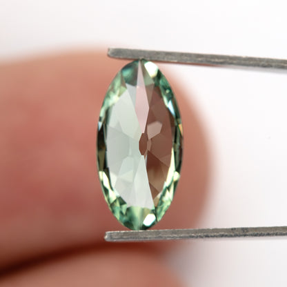 Back view of the mint-green lab-grown sapphire in tweezers against a fingertip.