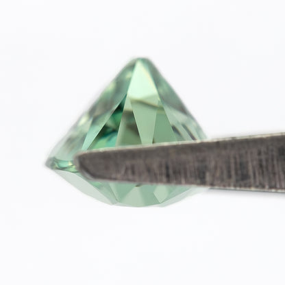 Pointed pavilion of the mint-green lab-grown sapphire seen obliquely between tweezer tips.