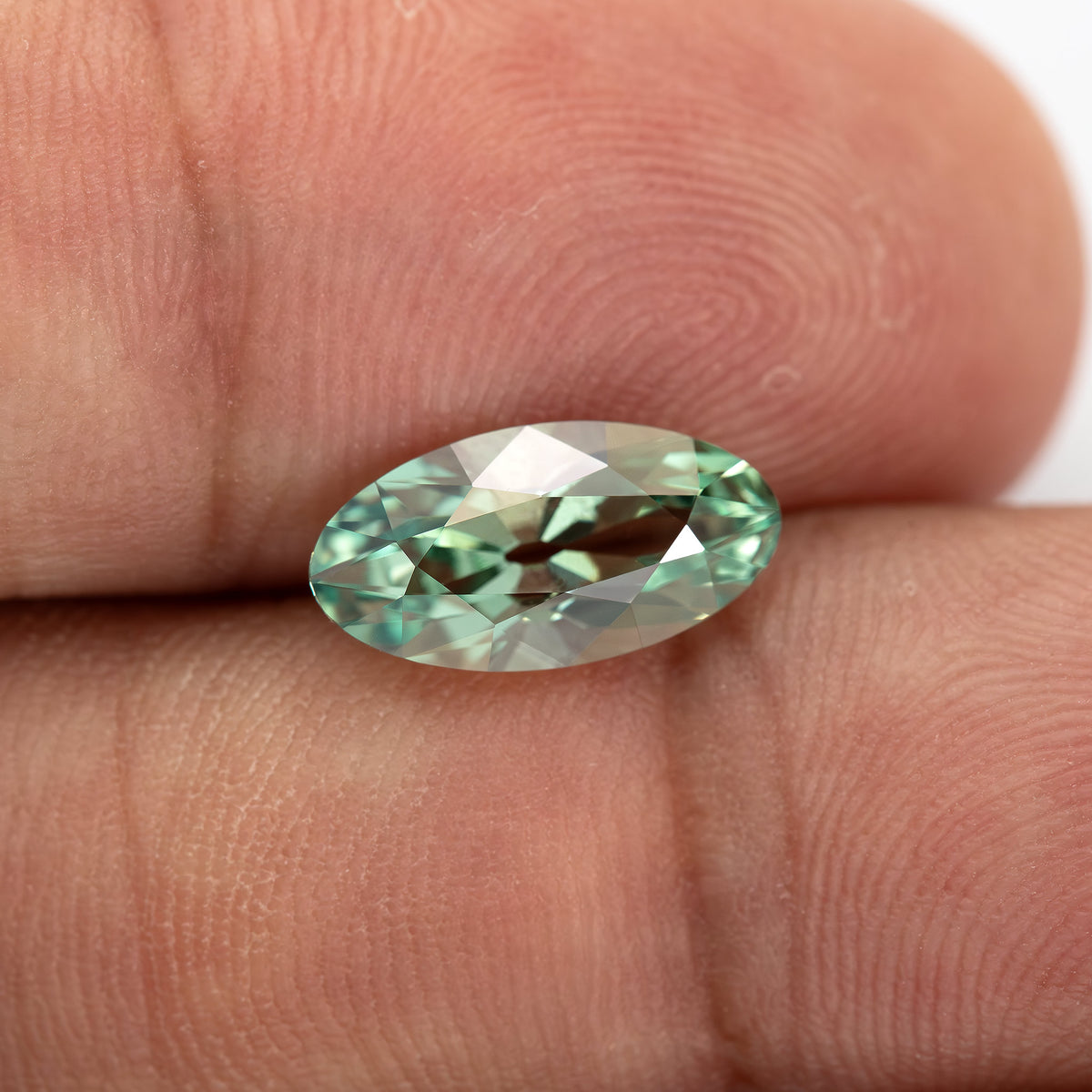 Mint-green lab-grown sapphire resting between fingertips at a low angle, showing its raised crown.