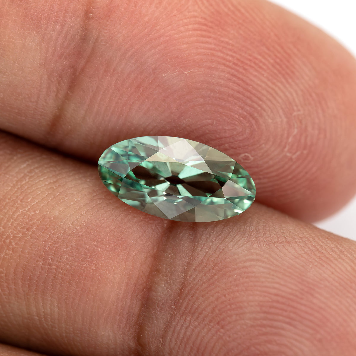 Mint-green lab-grown sapphire held between fingertips and tilted to show contrasting green facet reflections.