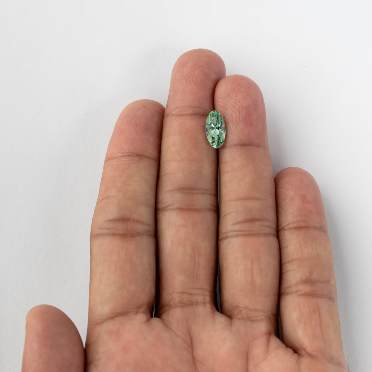 Small mint-green lab-grown sapphire resting on an open hand, giving wider real-life scale context.