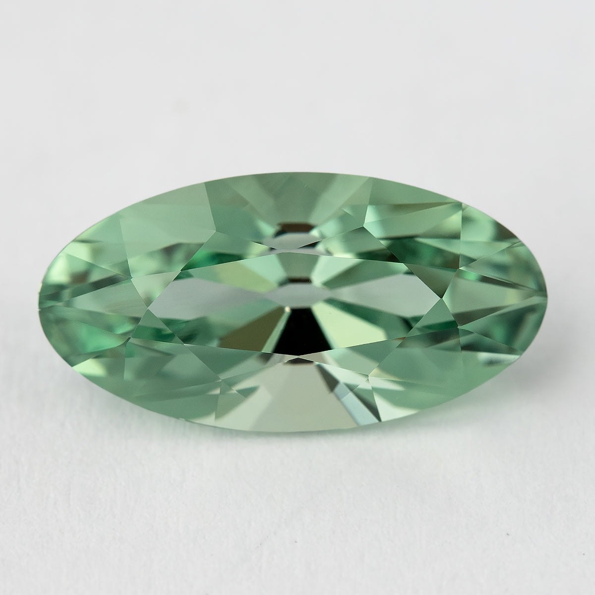 Horizontal face-up view of the mint-green lab-grown sapphire on a pale surface, with broad light and dark facets.