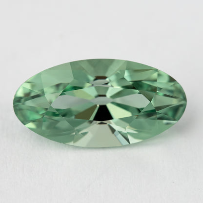 Horizontal face-up view of the mint-green lab-grown sapphire on a pale surface, with broad light and dark facets.