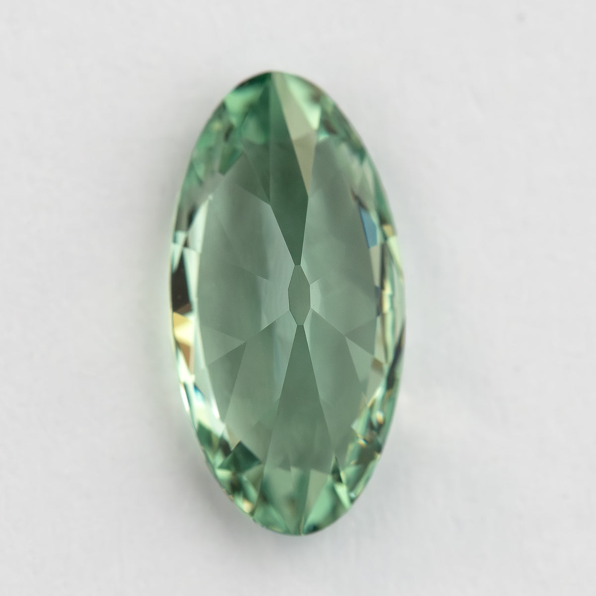 Vertical back view of the mint-green lab-grown sapphire resting on a pale surface.