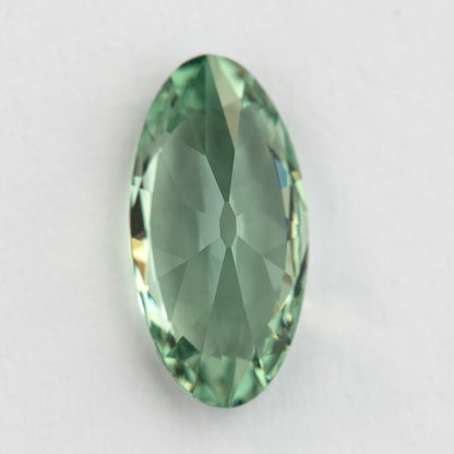 Vertical back view of the mint-green lab-grown sapphire resting on a pale surface.