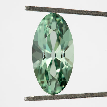 Mint-green lab-grown sapphire upright in tweezers, with crisp crown facets and the full outline visible.