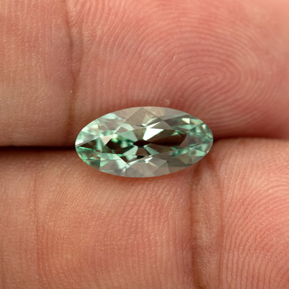 Mint-green lab-grown sapphire resting horizontally between fingertips, showing its broad face-up facets.