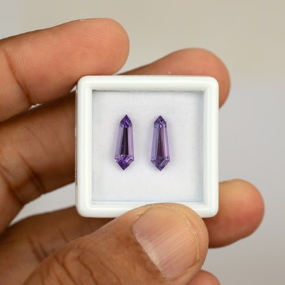 The purple sapphire pair in a handheld white display box, with both long pointed outlines visible.