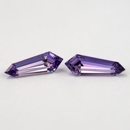 Two purple long-shield lab-grown sapphires at an angle on white, showing their broad tables and step-cut crown facets.