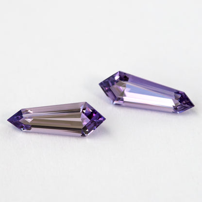 Two purple long-shield sapphires arranged diagonally on white, showing their pointed ends and broad step-cut faces.