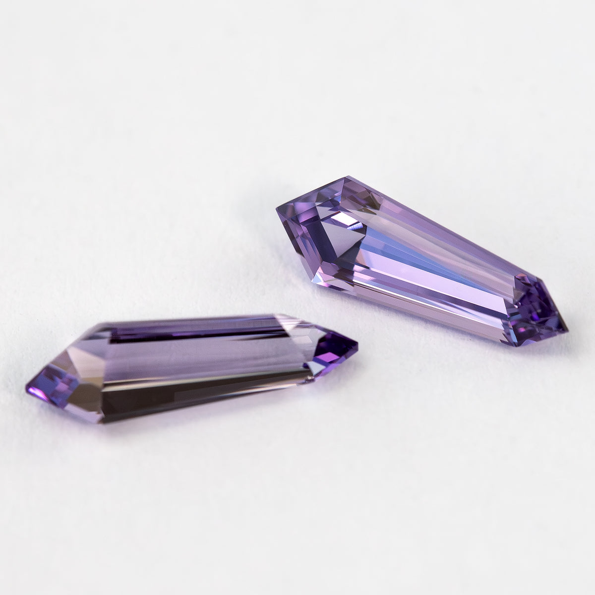 Closer angled view of the purple sapphire pair, with bright long reflections through the step-cut faces.