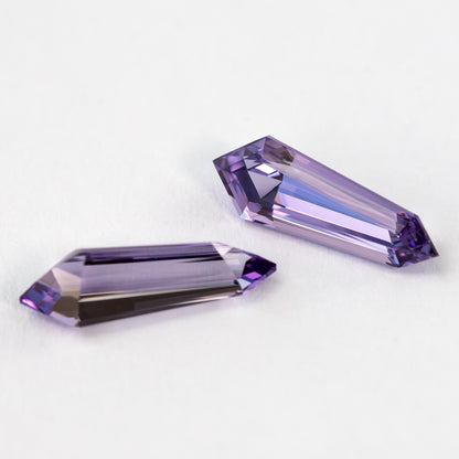 Closer angled view of the purple sapphire pair, with bright long reflections through the step-cut faces.