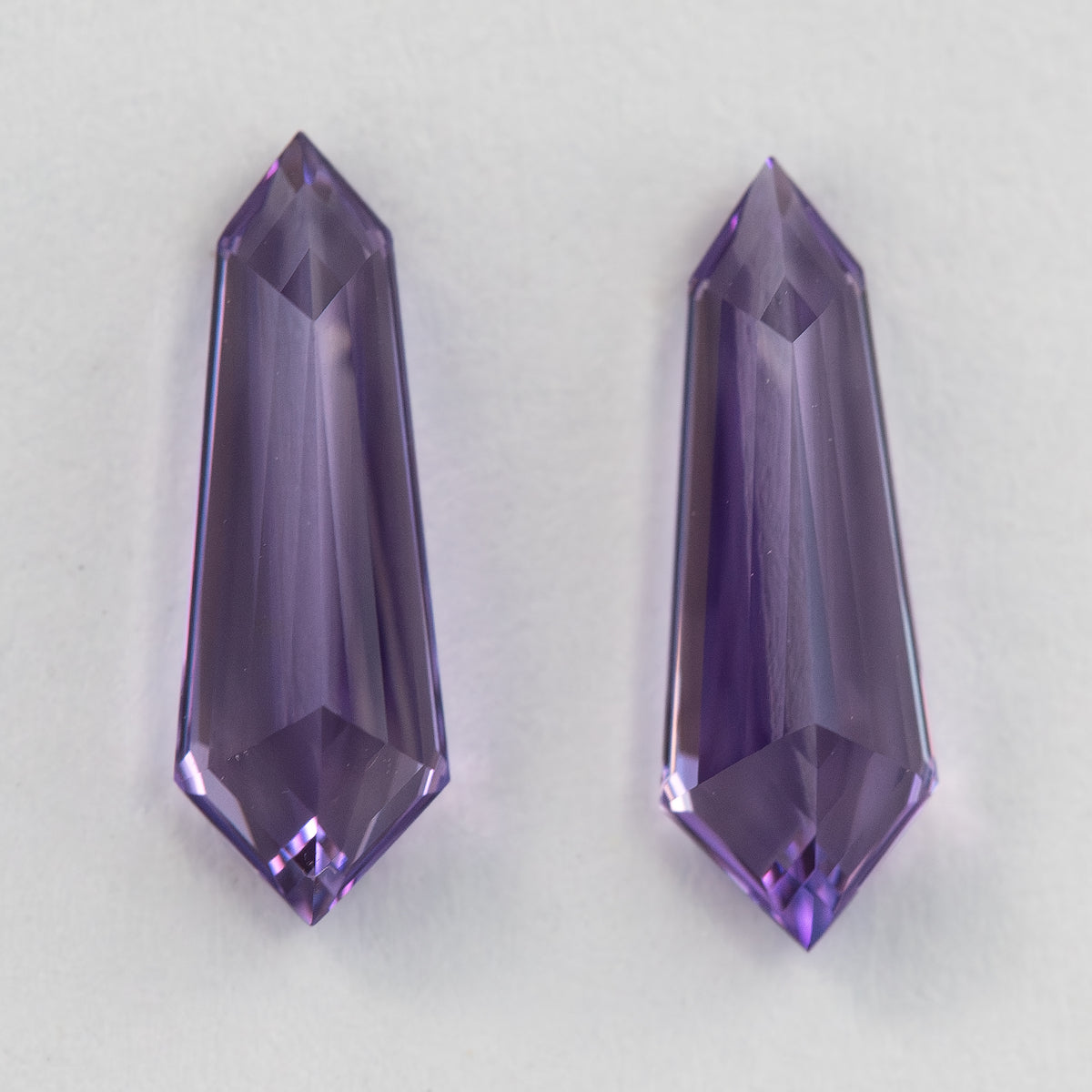 Opposite-side view of two purple long-shield sapphires placed vertically on white, showing pale central reflections.