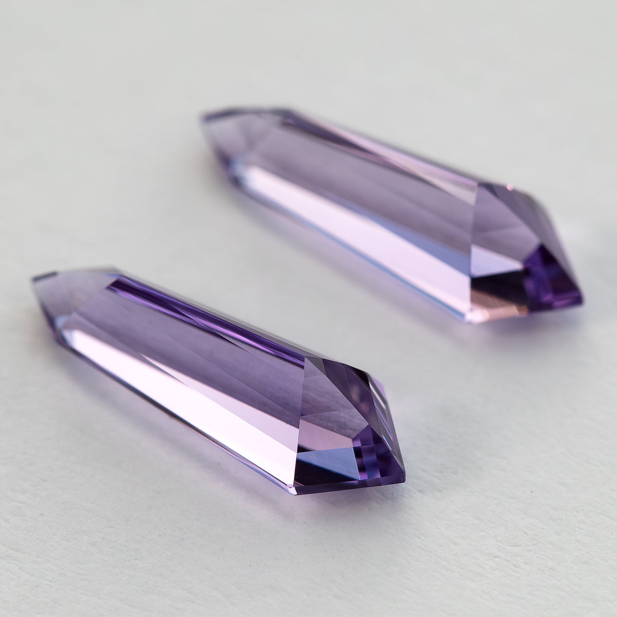 The purple long-shield sapphire pair tilted from the opposite side, with the underside facets visible.