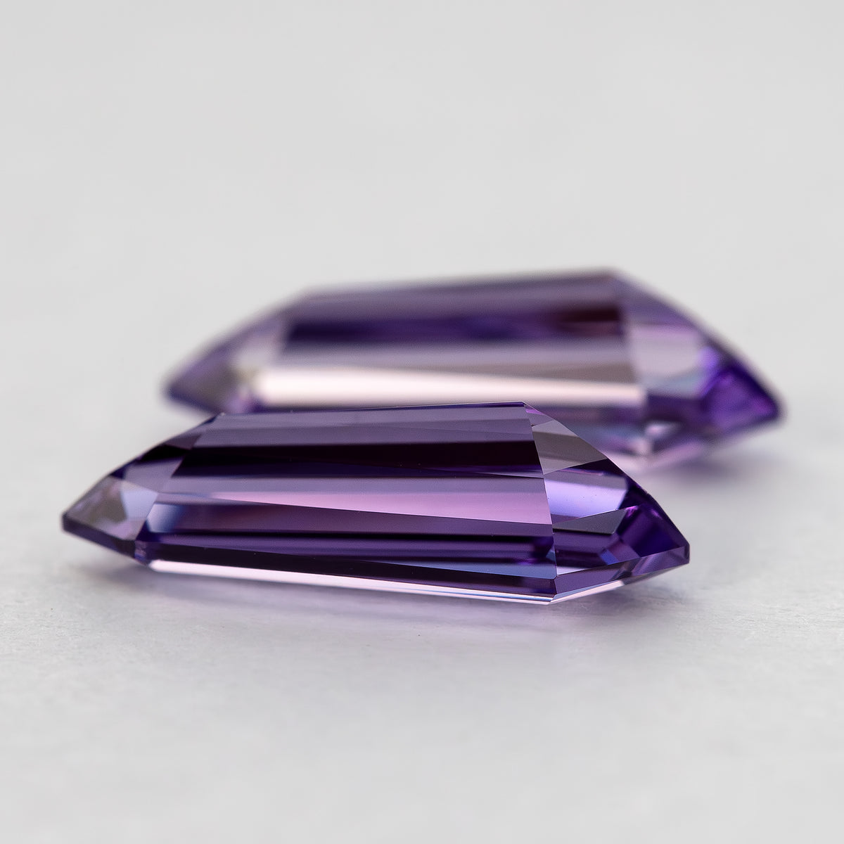 Very low side profile of two purple long-shield sapphires, emphasizing the height of the stepped faceting.