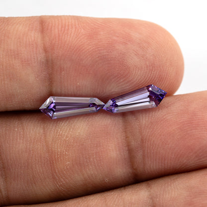 The purple long-shield sapphire pair on fingertips at a slightly different tilt, showing the scale of both stones.