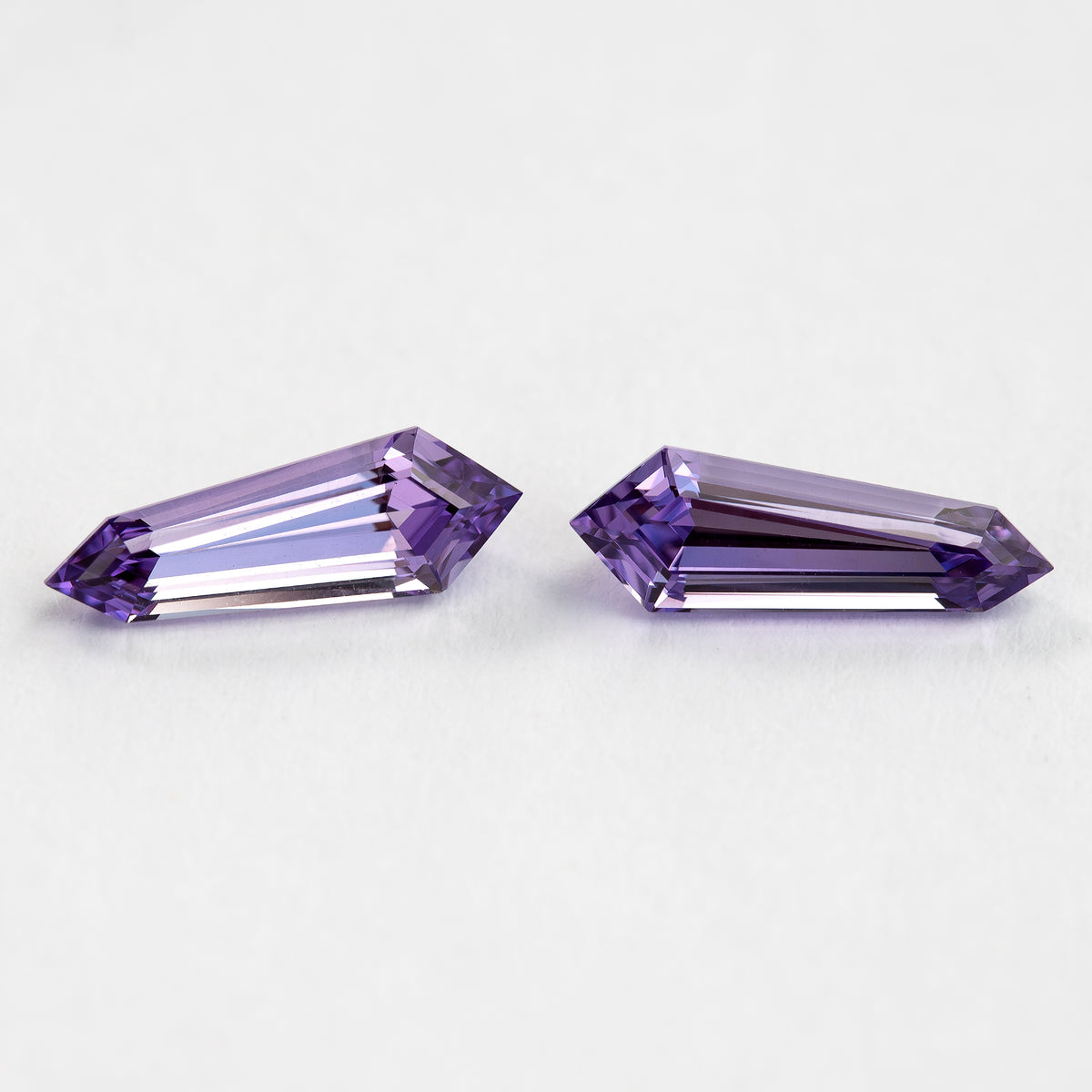 The purple long-shield sapphire pair face-up at an oblique angle, with brighter violet reflections near the pointed ends.