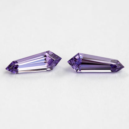The purple long-shield sapphire pair face-up at an oblique angle, with brighter violet reflections near the pointed ends.