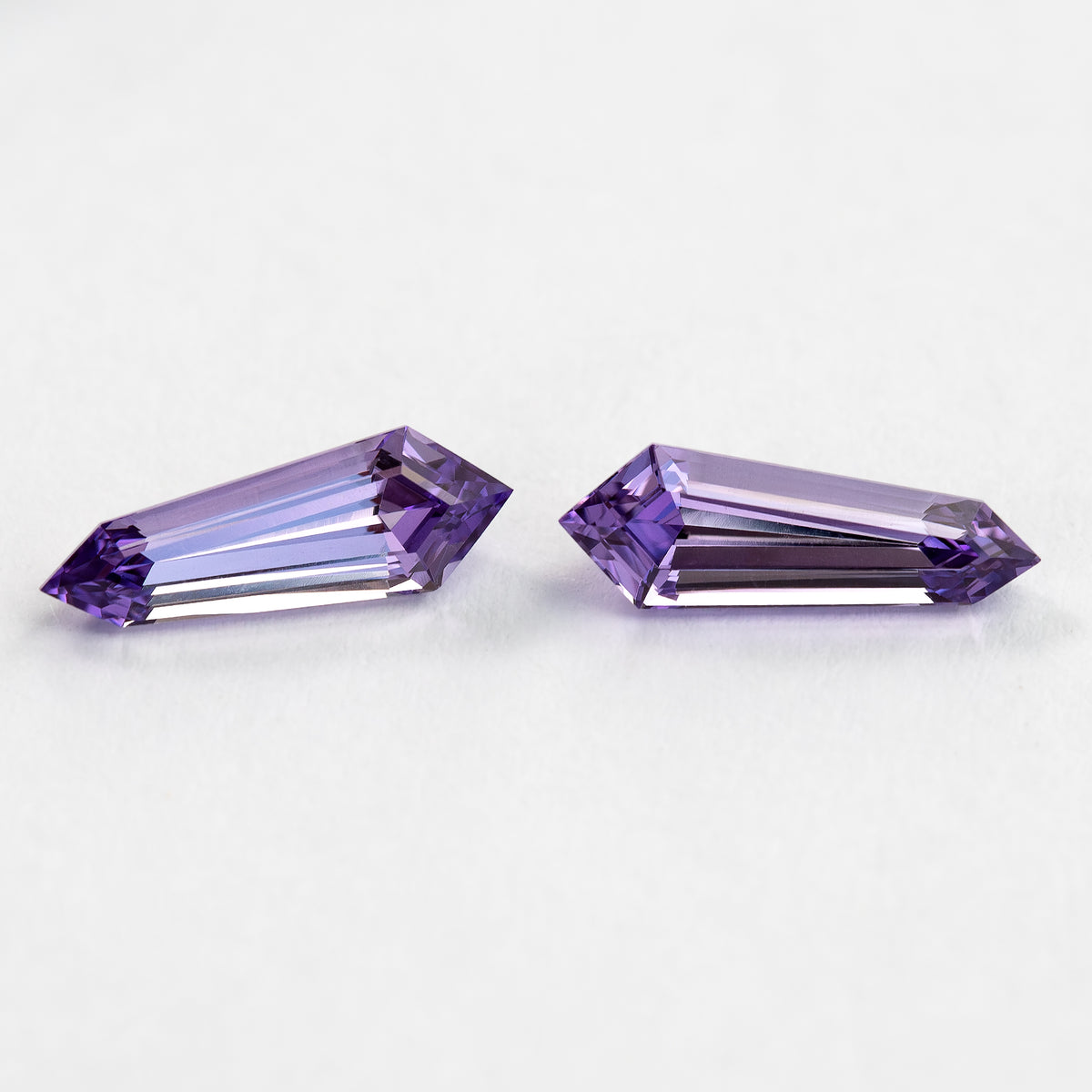 Two purple long-shield sapphires on white from another face-up angle, showing long pink-purple step reflections.