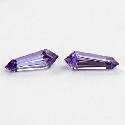 Two purple long-shield sapphires on white from another face-up angle, showing long pink-purple step reflections.